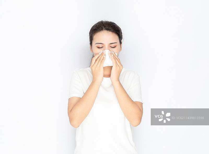 室内一名亚洲美女感冒用纸巾擦鼻子图片素材