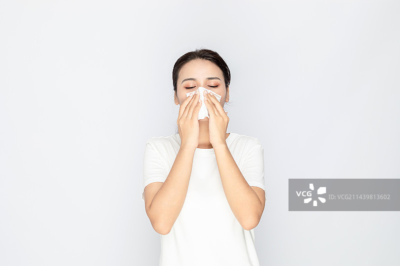 室内一名亚洲美女感冒用纸巾擦鼻子图片素材