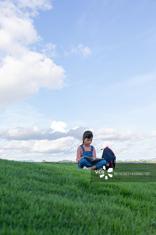 一名中国小女孩在草地上看书图片素材