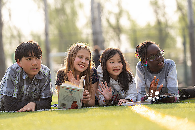 可爱的小学生们趴在草地上看书图片素材