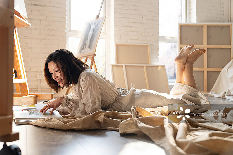工作室内趴在地上看书的青年画家图片素材