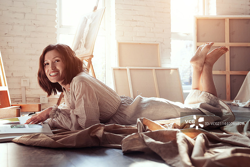 工作室内趴在地上看书的青年画家图片素材