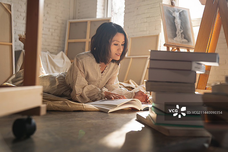 工作室内趴在地上看书的青年画家图片素材