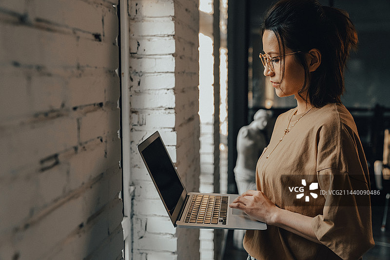 站在窗前使用笔记本电脑的青年设计师图片素材