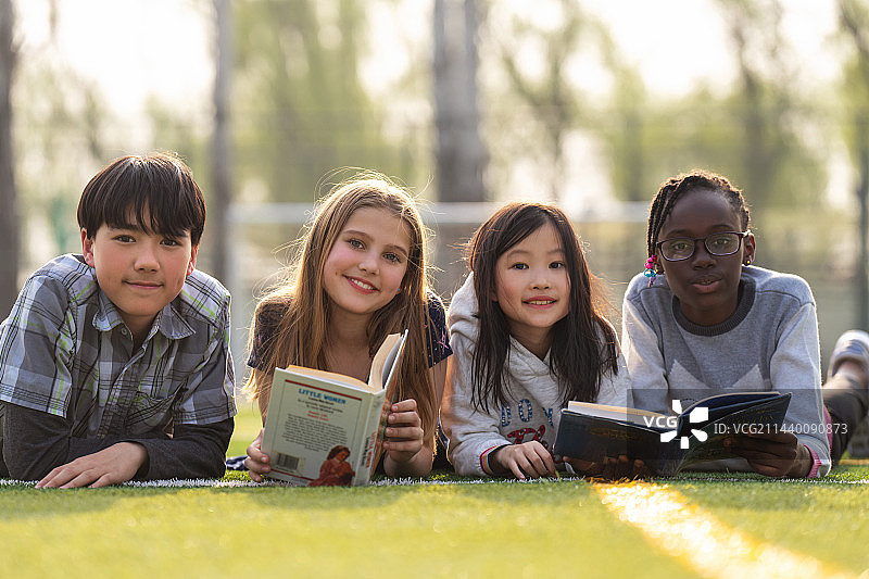 可爱的小学生们趴在草地上看书图片素材