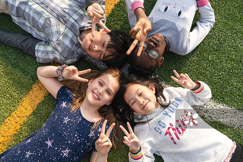 可爱的小学生们躺在草地上玩耍图片素材