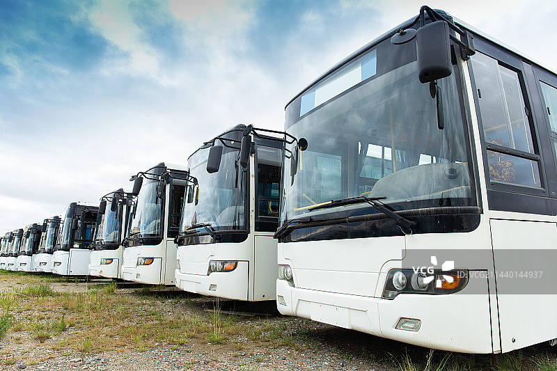许多干净的大巴车整齐地停靠在户外的草地停车场上图片素材