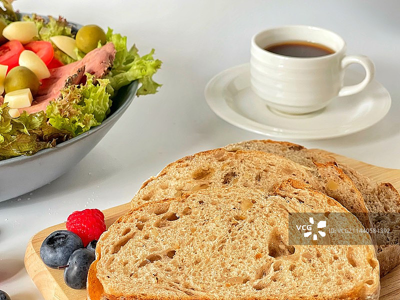 白色桌面上的切片面包及咖啡、水果、蔬菜沙拉图片素材