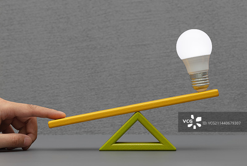 用手指翘起天平一端发亮的灯泡图片素材