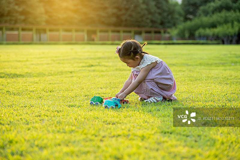 夕阳下公园草坪上一个玩玩具车的小女孩图片素材