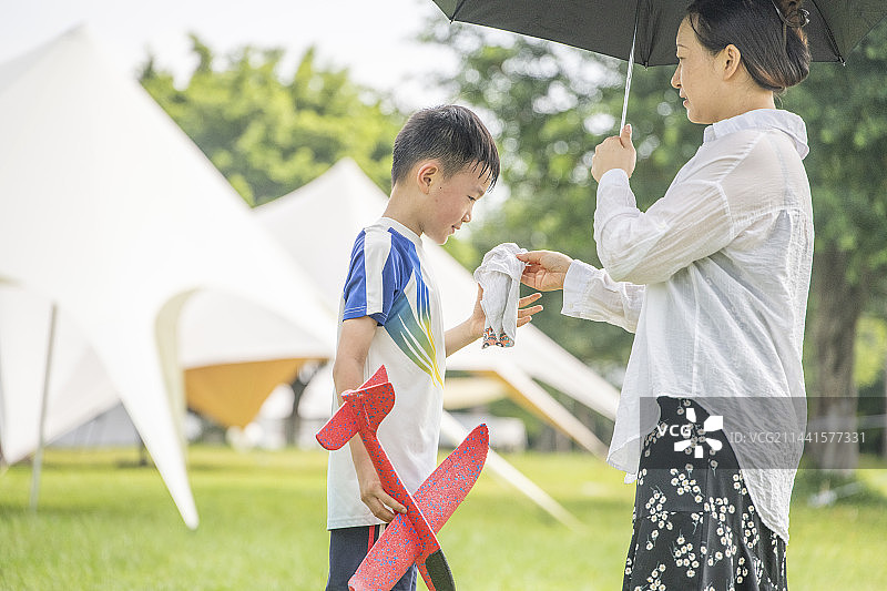 公园里的年轻妈妈正给孩子递毛巾擦汗图片素材