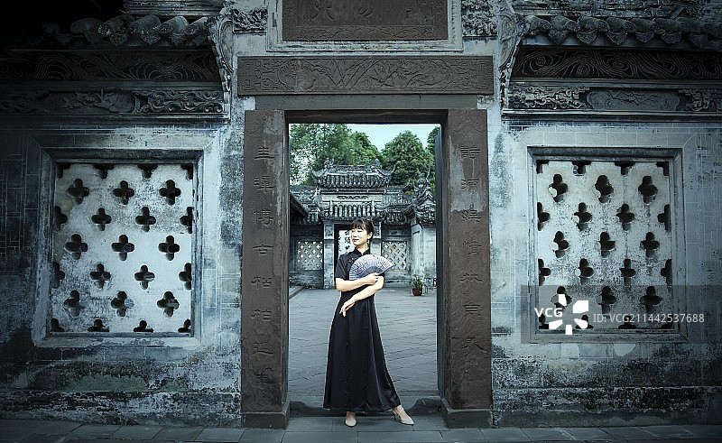 一位手里拿着扇子的漂亮女人站在一座古宅门口图片素材