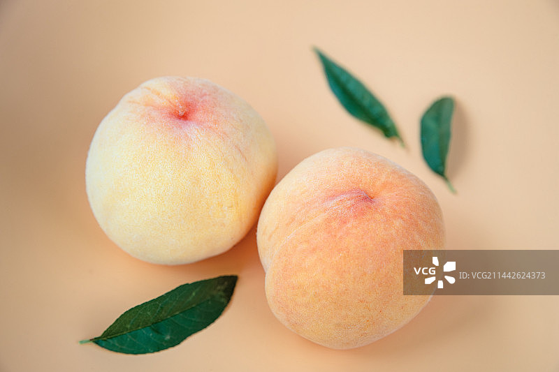 影棚俯视粉色背景上几片绿叶中两只成熟的桃子外观特写图片素材