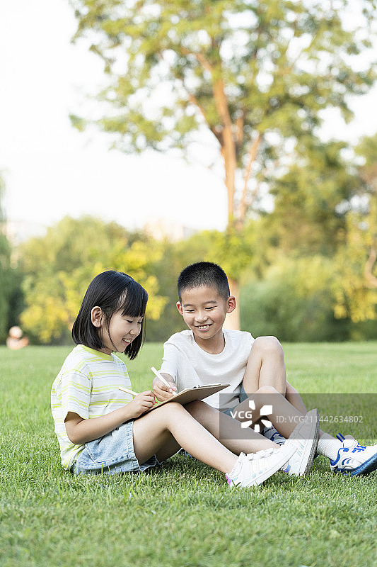 两名小学生坐在草地上交流学习图片素材