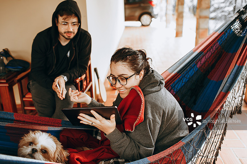 情侣在贝洛奥里藏特米纳斯吉拉斯州家中的吊床上放松身心，旁边有一只小宠物狗图片素材