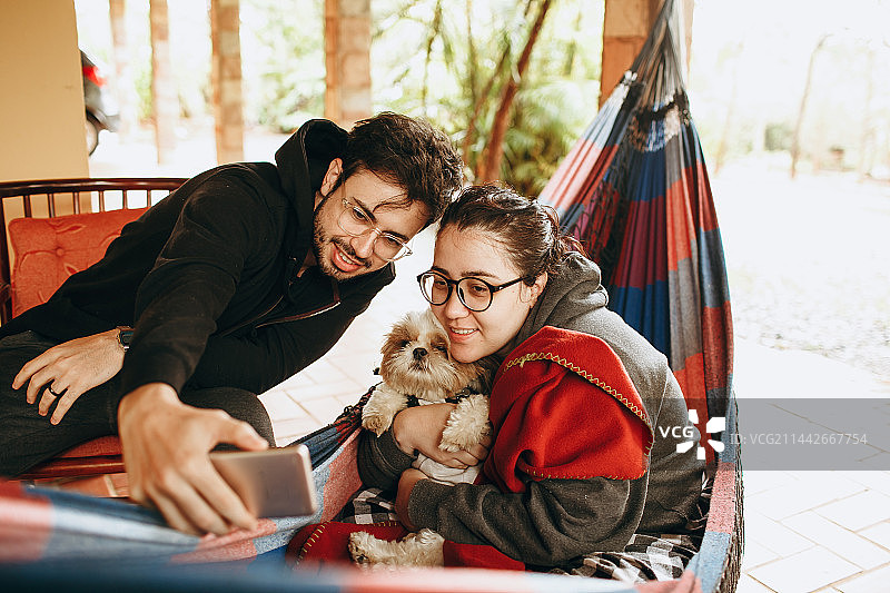 情侣在贝洛奥里藏特米纳斯吉拉斯州家中的吊床上放松身心，旁边有一只小宠物狗图片素材