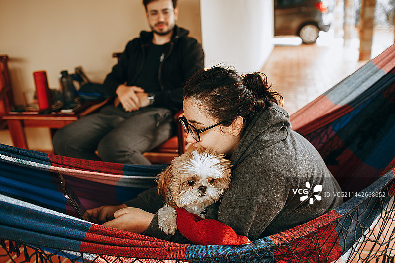 情侣在贝洛奥里藏特米纳斯吉拉斯州家中的吊床上放松身心，旁边有一只小宠物狗图片素材