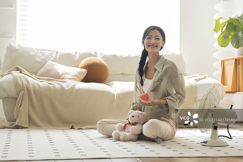 青年女子在客厅吹电风扇、吃西瓜图片素材