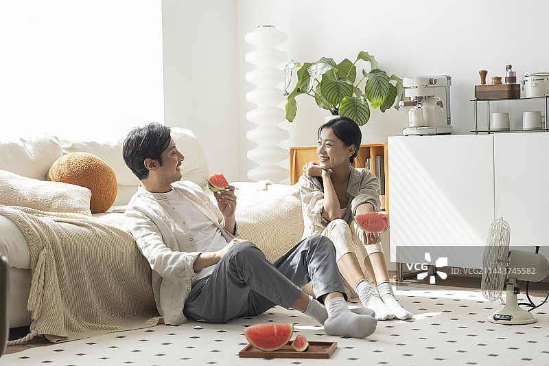 年轻情侣在客厅吃西瓜、吹电风扇、聊天图片素材