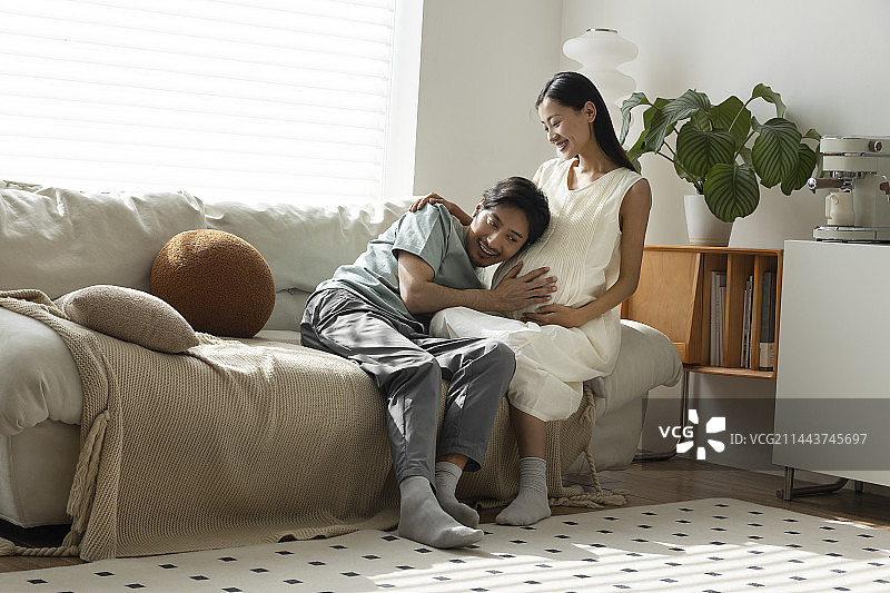 年轻丈夫在客厅听妻子的孕肚图片素材