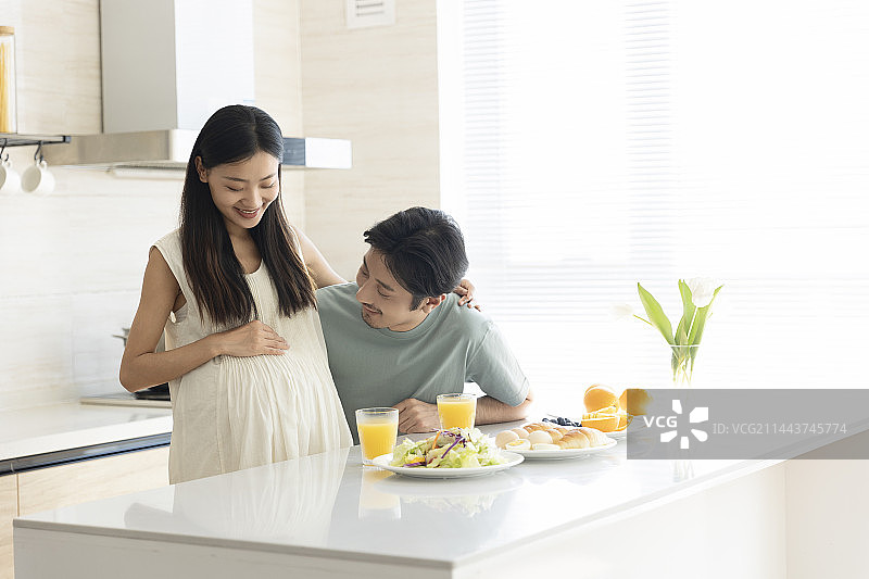 丈夫和怀孕妻子在开敞厨房吃早餐、与孕肚中的新生儿互动图片素材