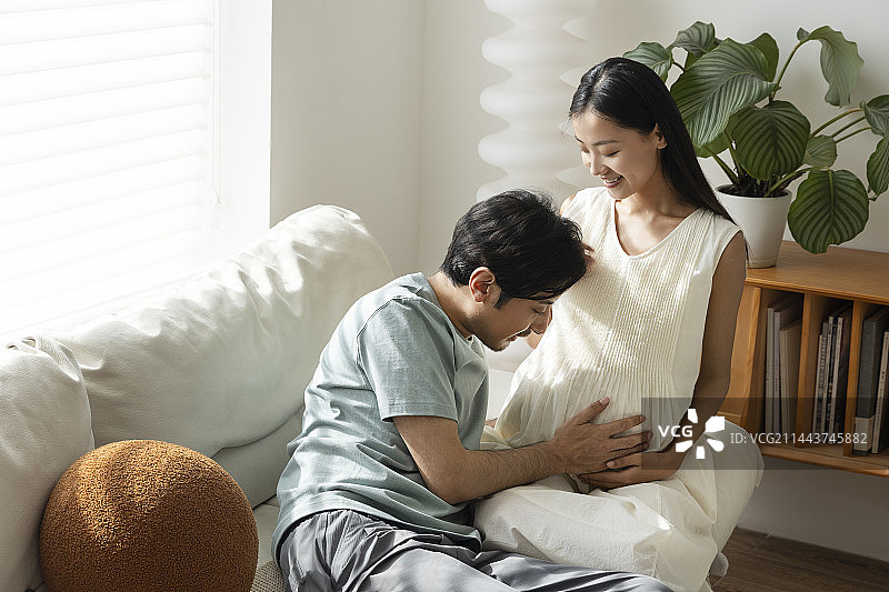 年轻丈夫在客厅抚摸妻子的孕肚图片素材