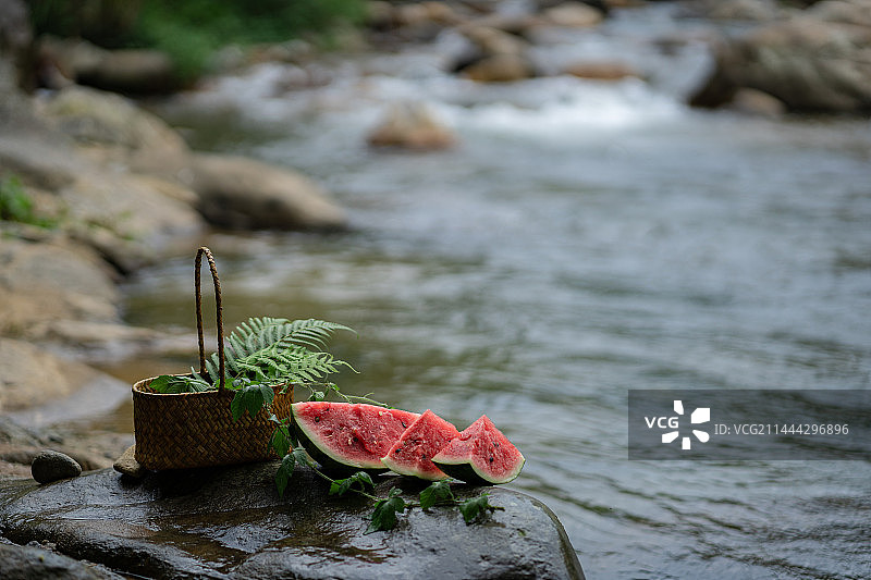 户外溪边石头上的消暑佳品西瓜与装满绿植的篮子图片素材