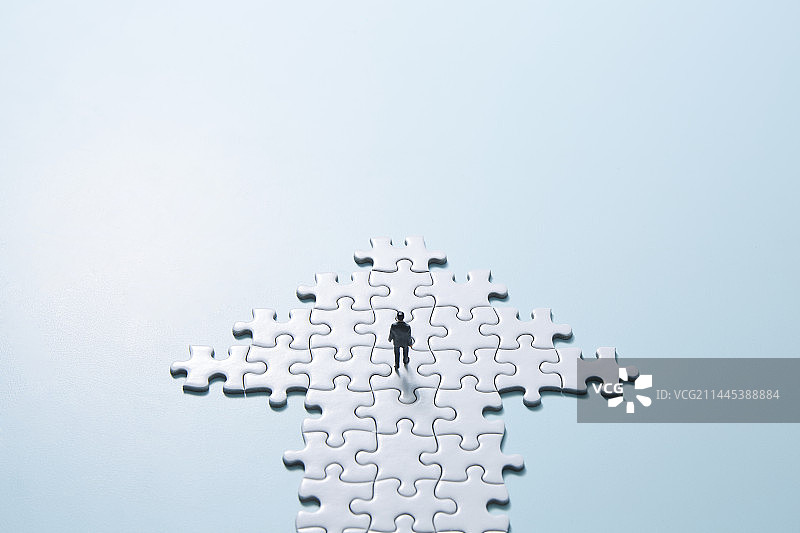 微型娃娃在浅蓝色背景和白色拼图箭头中行走图片素材