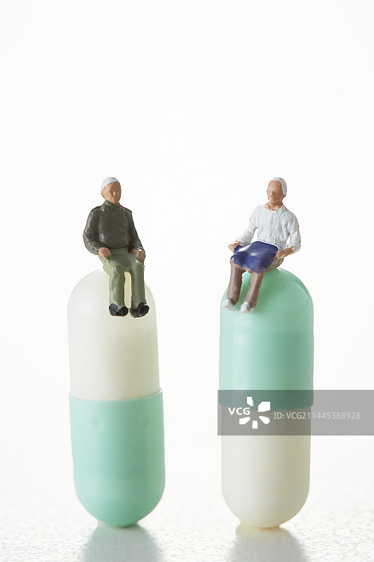 坐在胶囊药丸上的两个微型老人图片素材