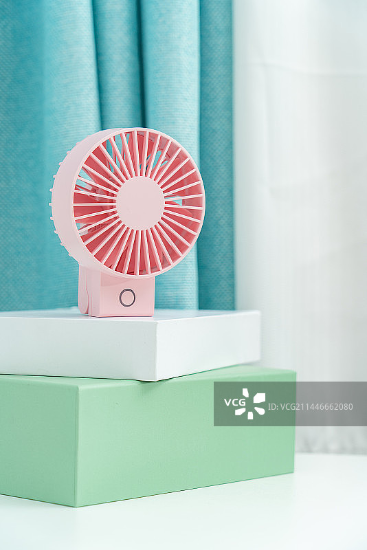 一台粉色的电扇放在蓝色窗帘前图片素材