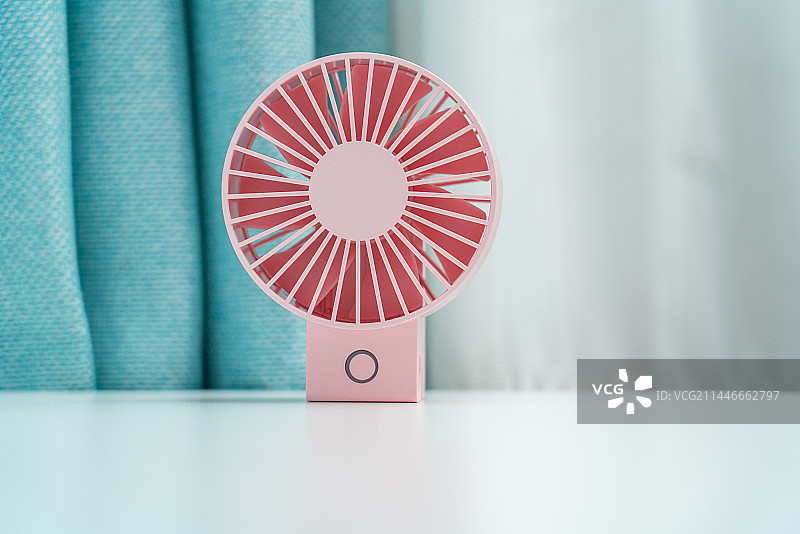 一台粉色的电扇放在蓝色窗帘前图片素材