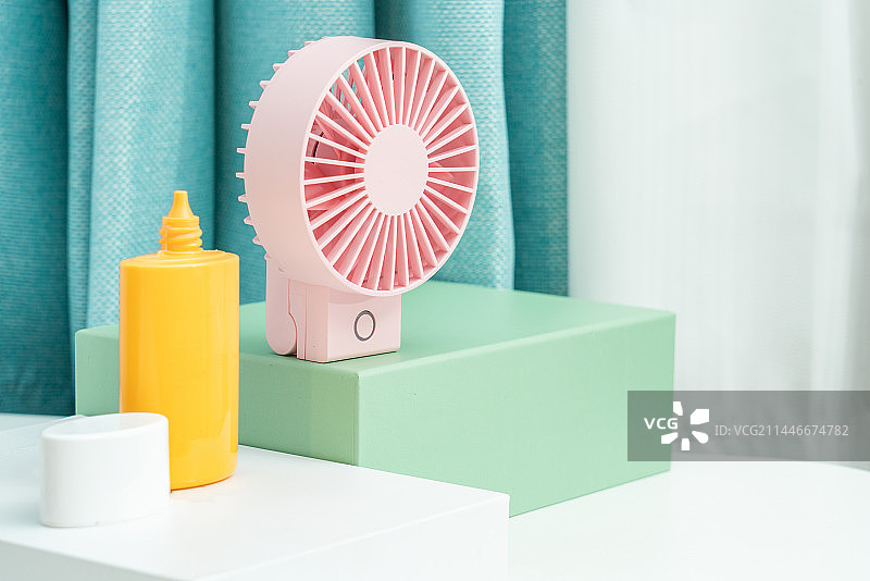粉色的电扇和防晒乳放在白色桌面上图片素材