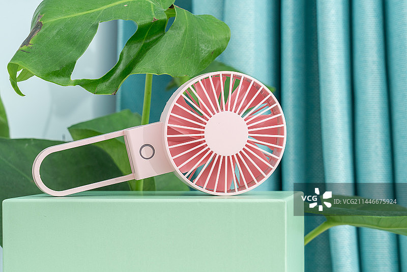 一台粉红色电扇放在绿色植物前图片素材