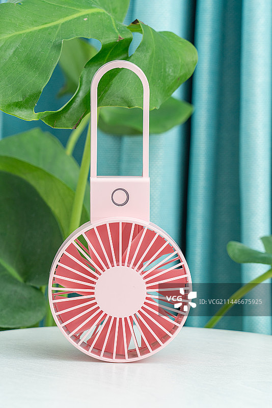 一台粉红色电扇放在绿色植物前图片素材