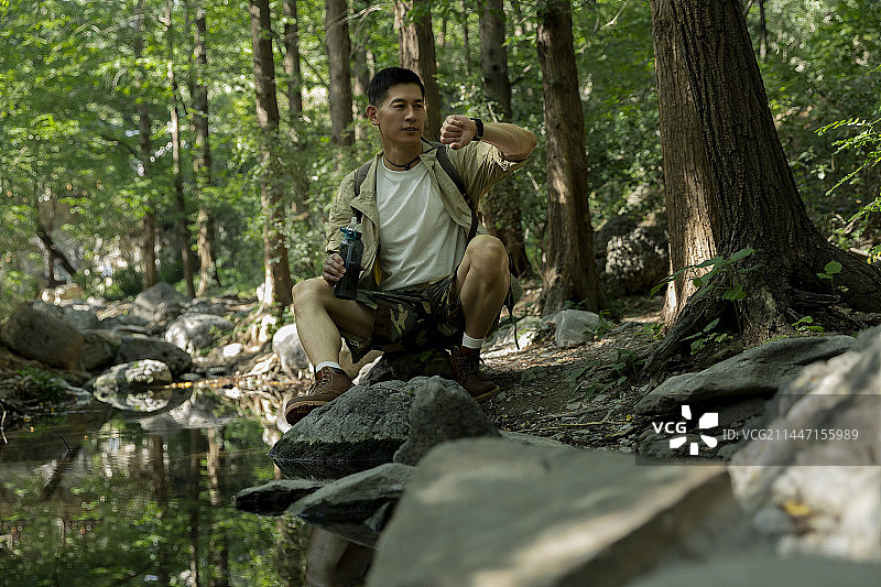 徒步旅行者坐在杉树森林中的小河边看手表图片素材