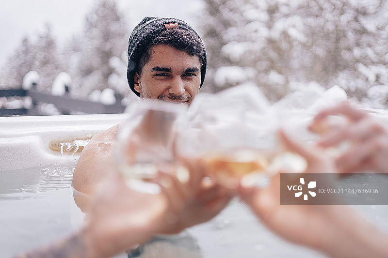 年轻男人在威斯康星州双子湖的冬季热水浴缸中与朋友举杯庆祝图片素材