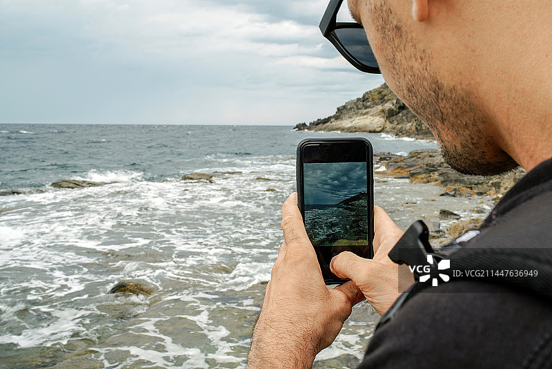 在西班牙赫罗纳的塞尔瓦港，男子用手机拍摄大海图片素材