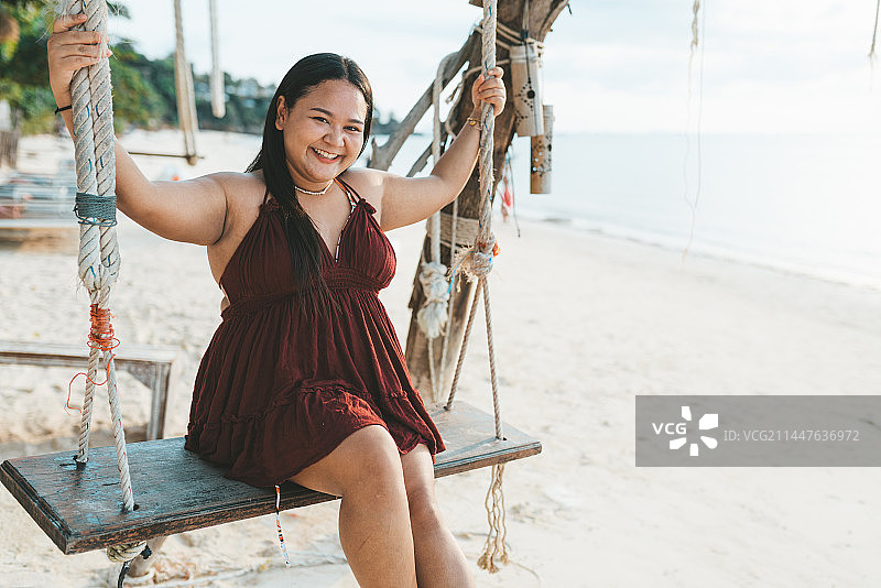 白天在海滩上穿着红色连衣裙的曲线玲珑的年轻女人肖像图片素材