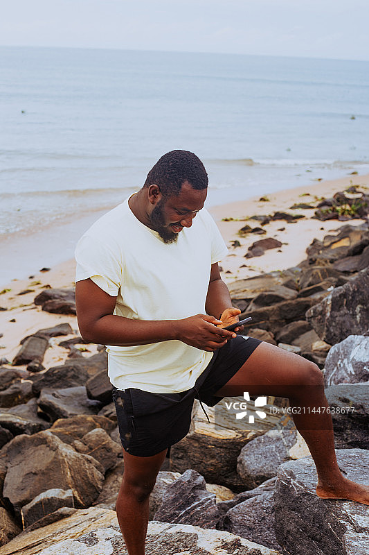 在加纳阿克拉海滩站着使用手机的年轻男人图片素材