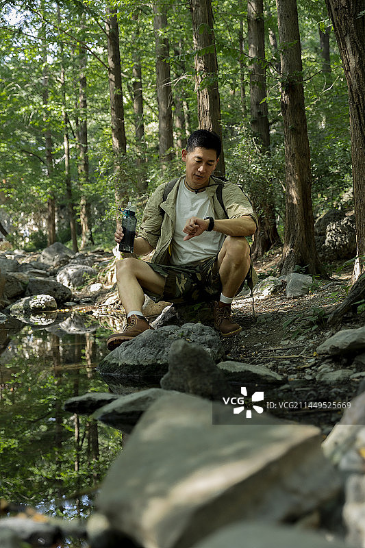 徒步旅行者坐在杉树森林中的小河边看手表图片素材