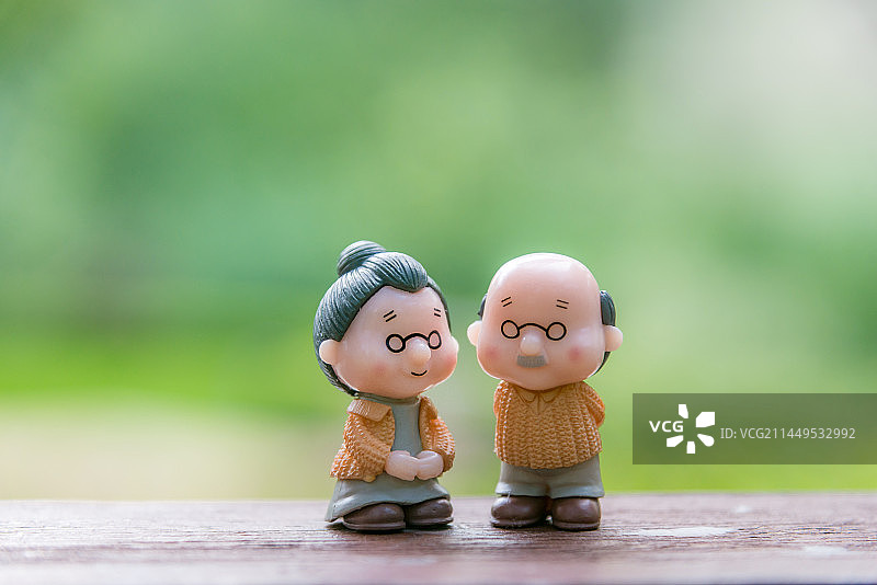 养老 老年生活概念：老年夫妇人偶在户外晒太阳，绿色背景图片素材