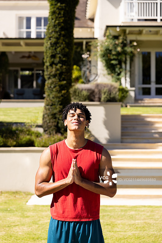 在房子前的院子里闭着眼睛祈祷的英俊混血年轻人图片素材