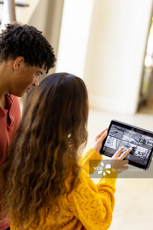 年轻的混血夫妇用平板电脑通过摄像机控制家居图片素材