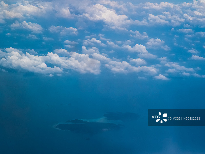 白云下，无边的蓝色海面上的岛屿。图片素材