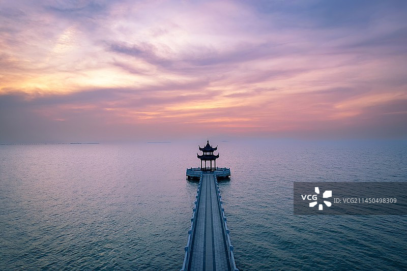 清晨时分天边挂着五颜六色的朝霞，温暖的阳光笼罩在太湖湖面，一条栈道向湖面延伸，尽头是古色古香的望湖亭图片素材
