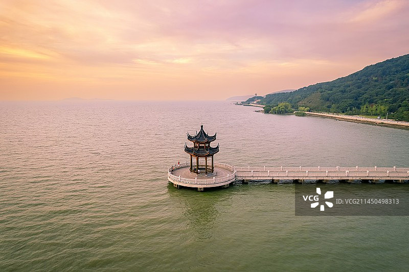 清晨时分天边挂着五颜六色的朝霞，温暖的阳光笼罩在太湖湖面，一条栈道向湖面延伸，尽头是古色古香的望湖亭图片素材