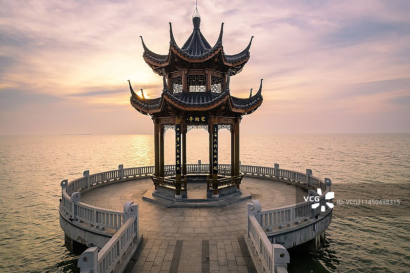 清晨时分天边挂着五颜六色的朝霞，温暖的阳光笼罩在太湖湖面，一条栈道向湖面延伸，尽头是古色古香的望湖亭图片素材