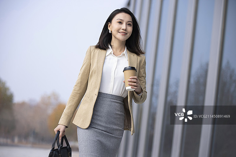 Confident businesswoman walking with a cup of coffee图片素材