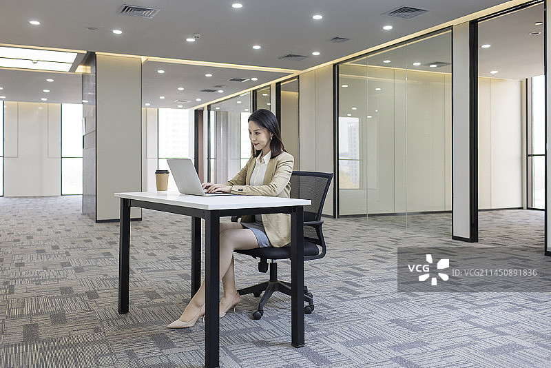 Confident businesswoman using laptop in empty office图片素材