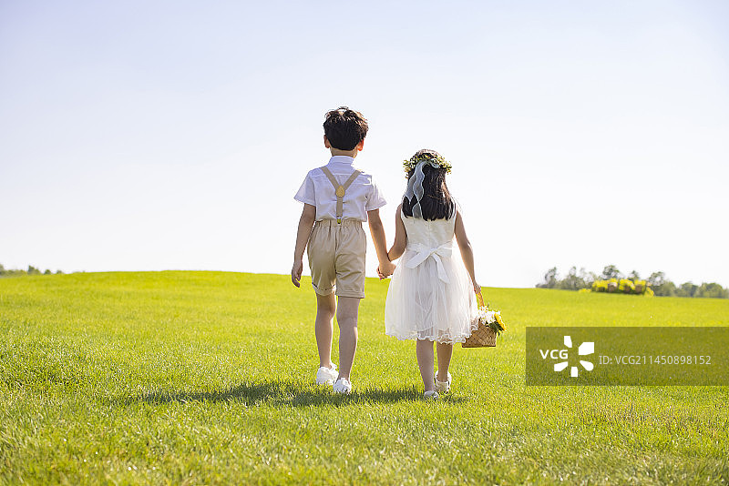 Cute flower girl and ring bearer playing on the grass图片素材